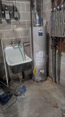 A water heater next to a utility sink in a concrete basement.