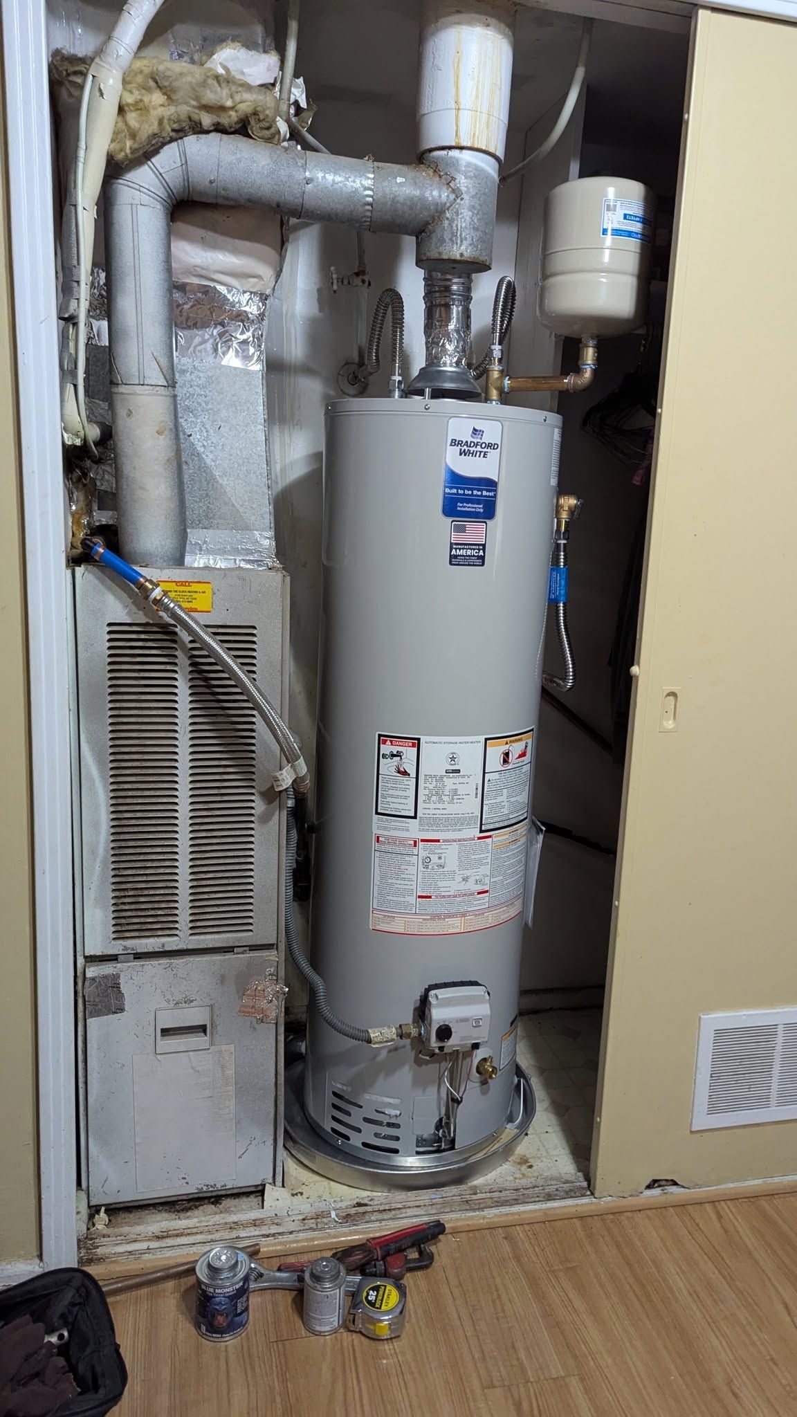 Water heater and furnace in a utility closet with exposed pipes and venting.