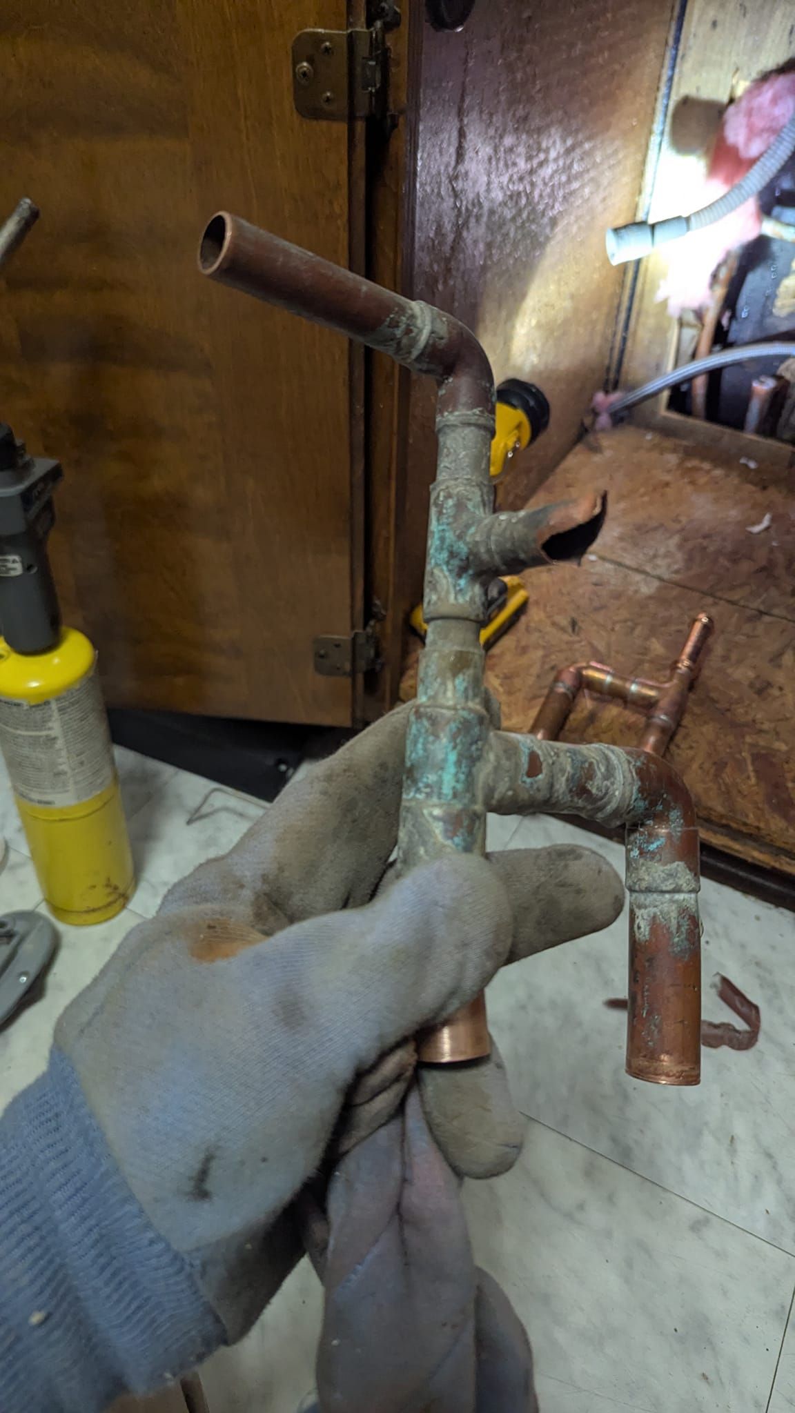 A person wearing gloves holds a corroded copper pipe assembly, possibly for plumbing repair.