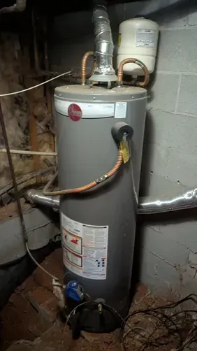 Gray water heater in a basement with pipes and an expansion tank mounted above it.