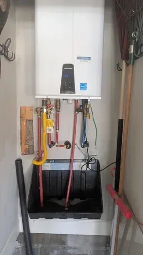 Wall-mounted boiler with exposed red, yellow, and blue pipes in a utility closet.