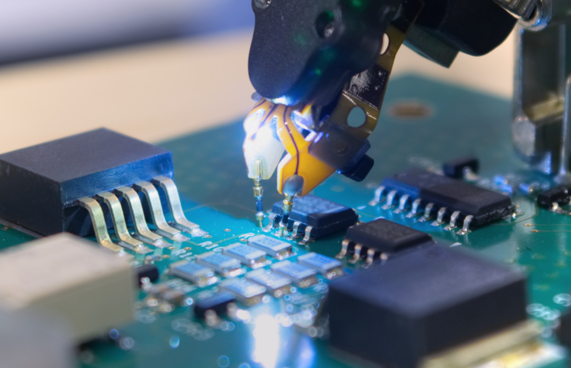Robotic arm soldering components on a circuit board with bright blue light