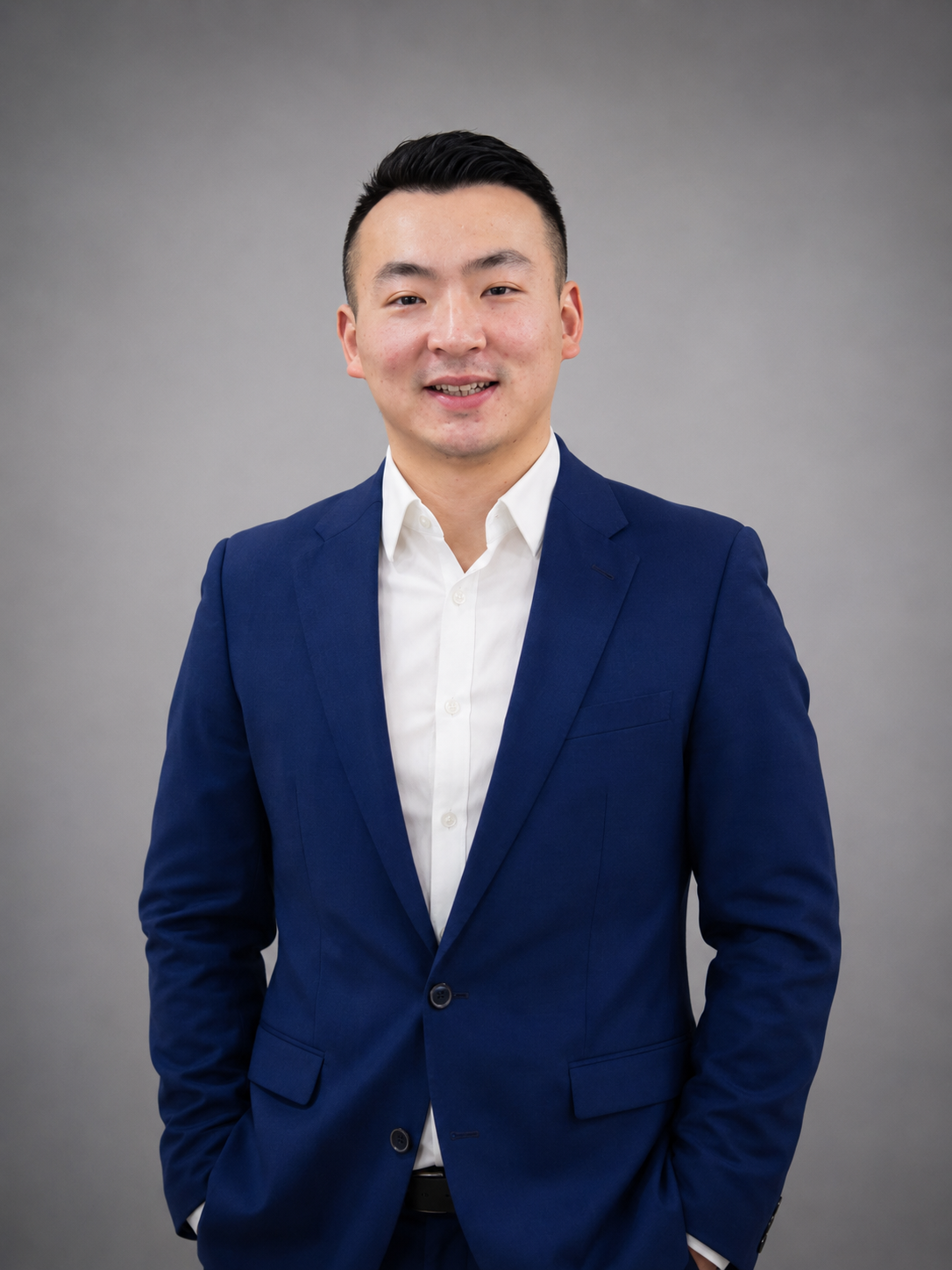 Man in blue suit, hands in pockets, smiling. Standing in front of a wood-paneled wall.
