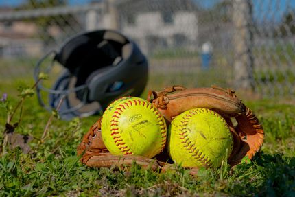 Baseball glove with ball on green grass, with blurred baseballs in the background.