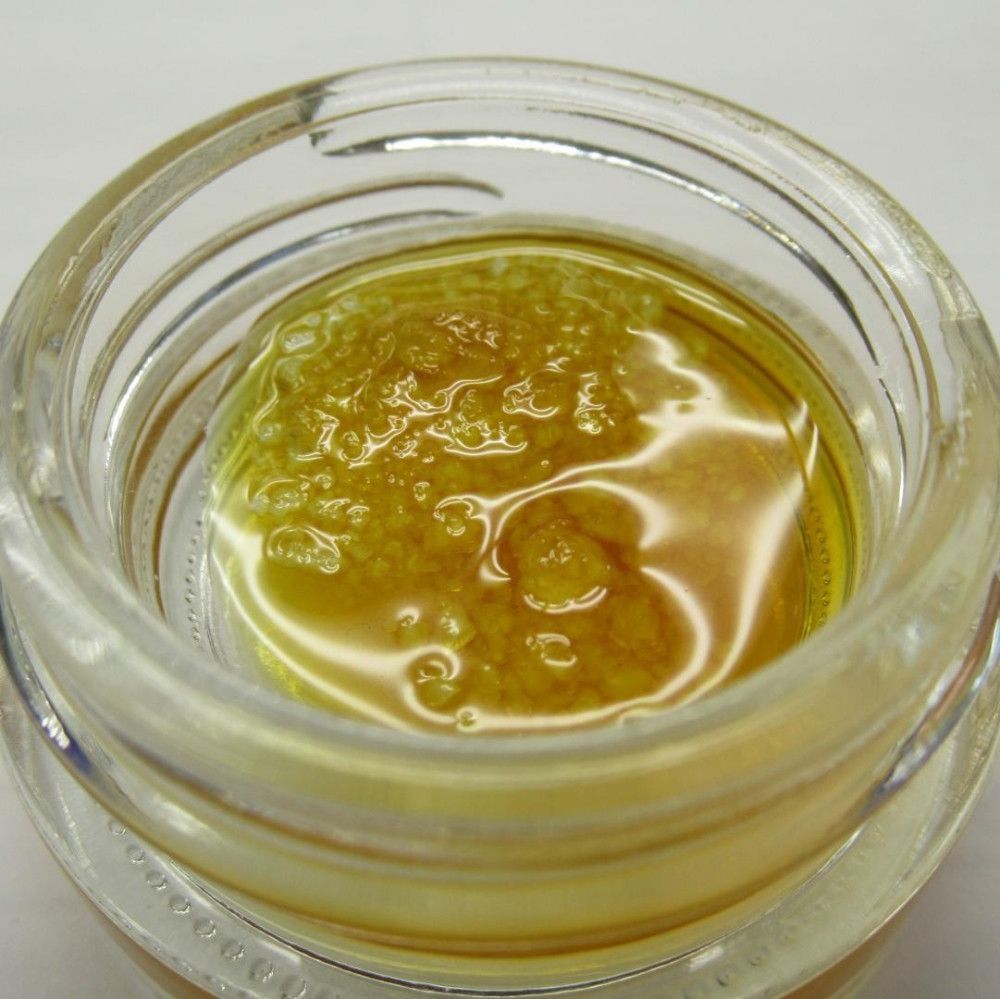 A close-up of cannabis concentrate in a glass jar; yellow-brown, oily texture.