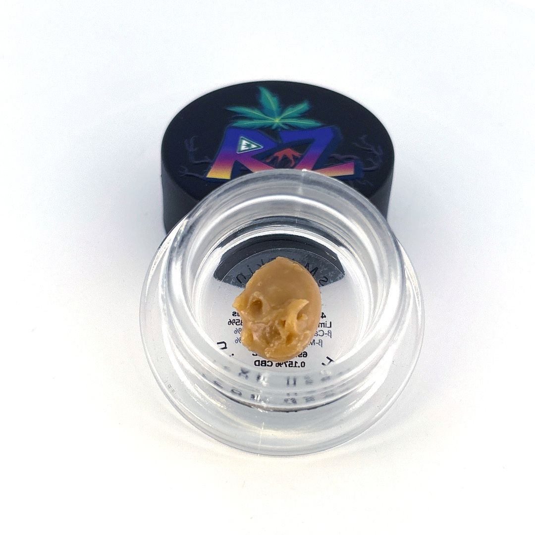 Cannabis concentrate in a small clear jar; dark cap with logo in background.