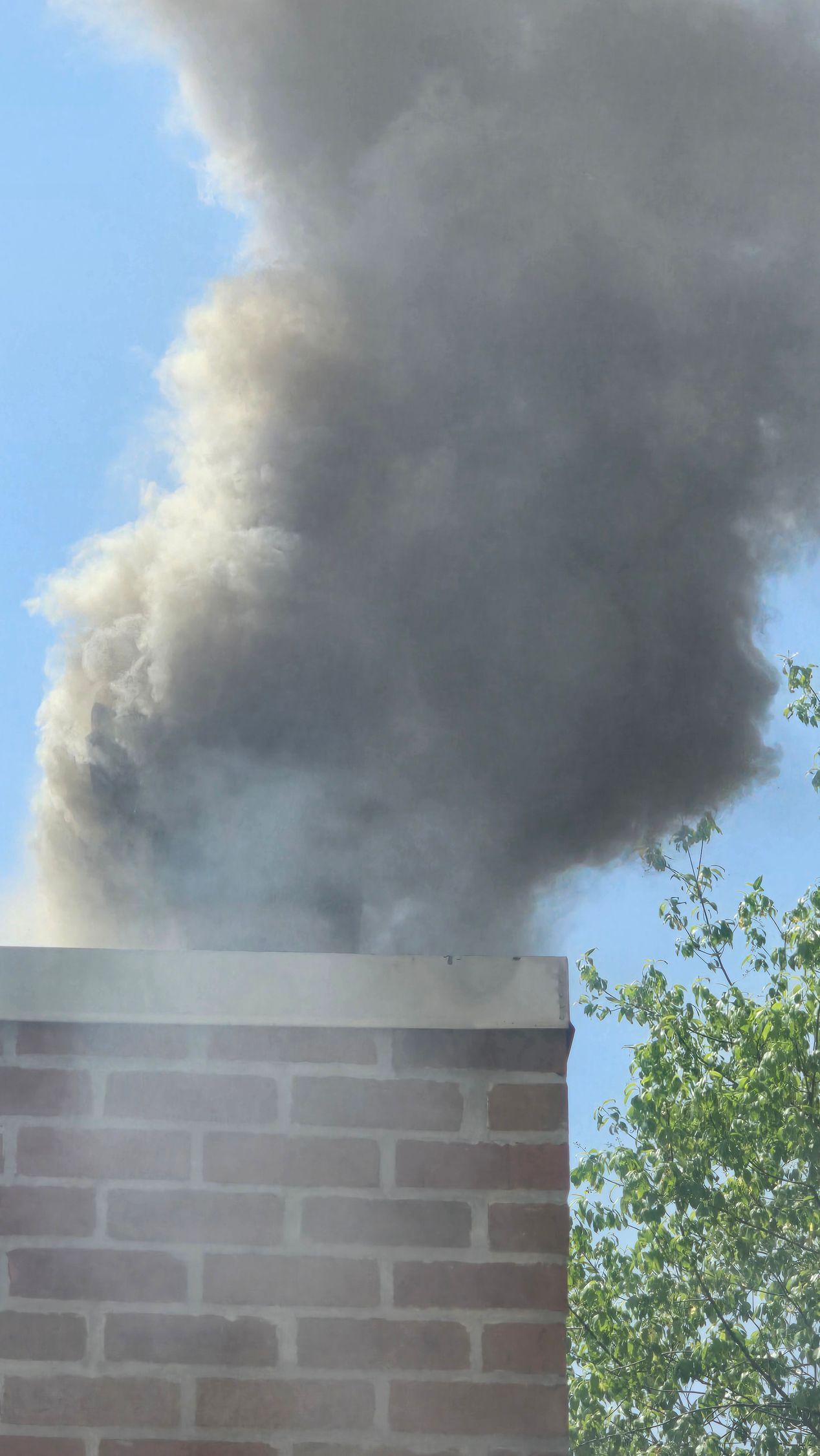Thick gray smoke billowing from a brick chimney against a blue sky
