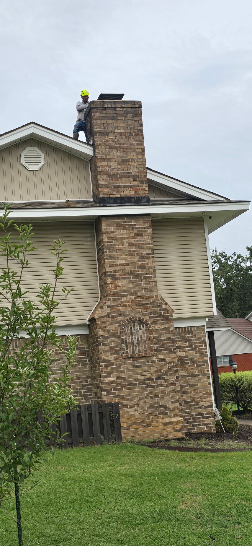 Brick chimney on a beige house roof with a person in a yellow hard hat inspecting it