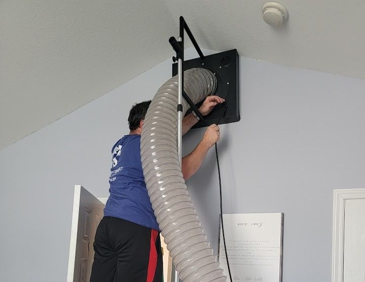Person cleaning a ceiling vent with a vacuum hose attachment indoors