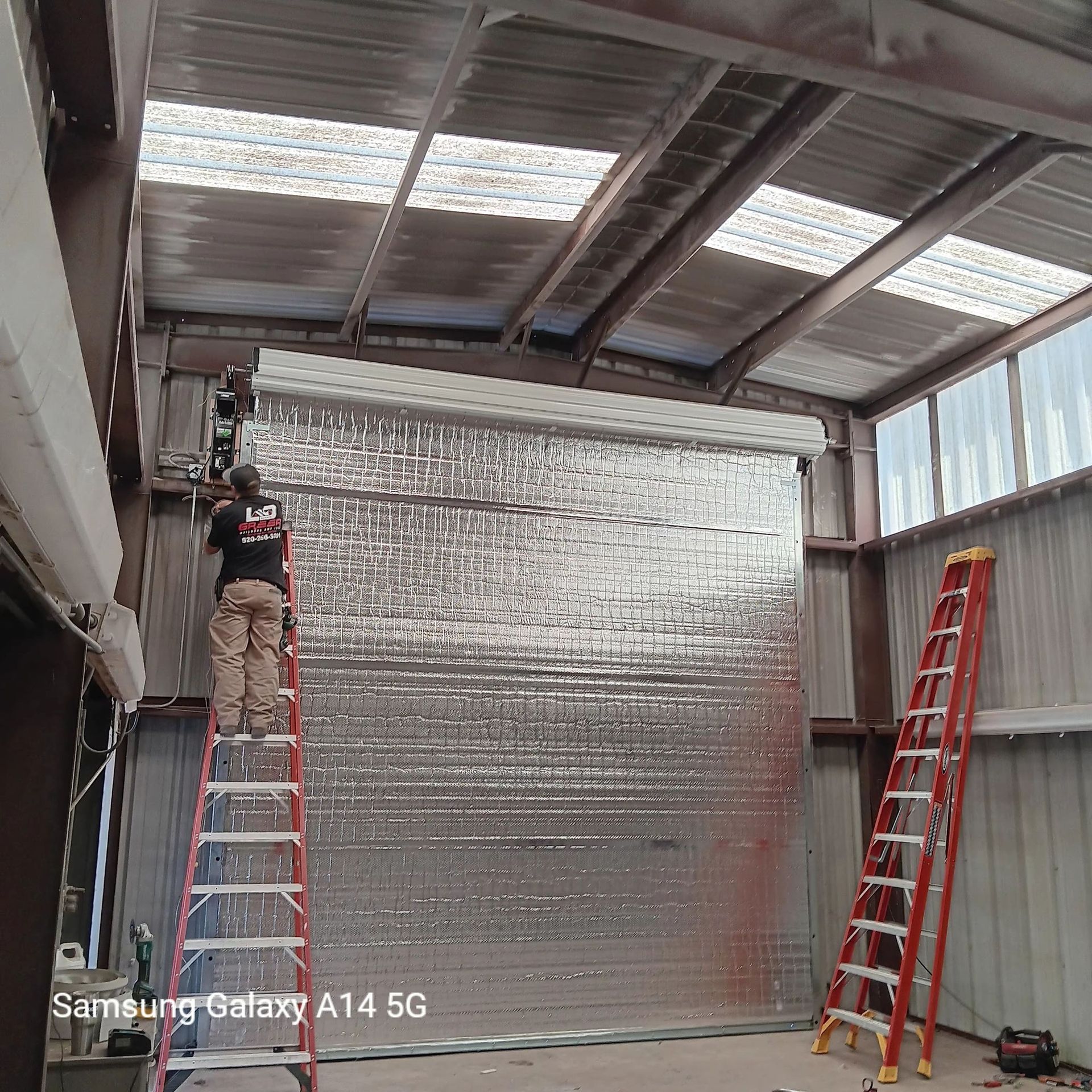 A man on a ladder is working on a garage door.