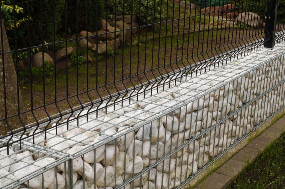 A Stone Wall with A Metal Fence Surrounding It — Rearden Fencing Pty Ltd in Toronto, NSW