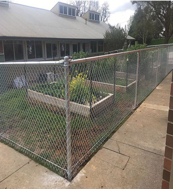 A Chain Link Fence Surrounds a Garden in Front of a House — Rearden Fencing Pty Ltd in Toronto, NSW