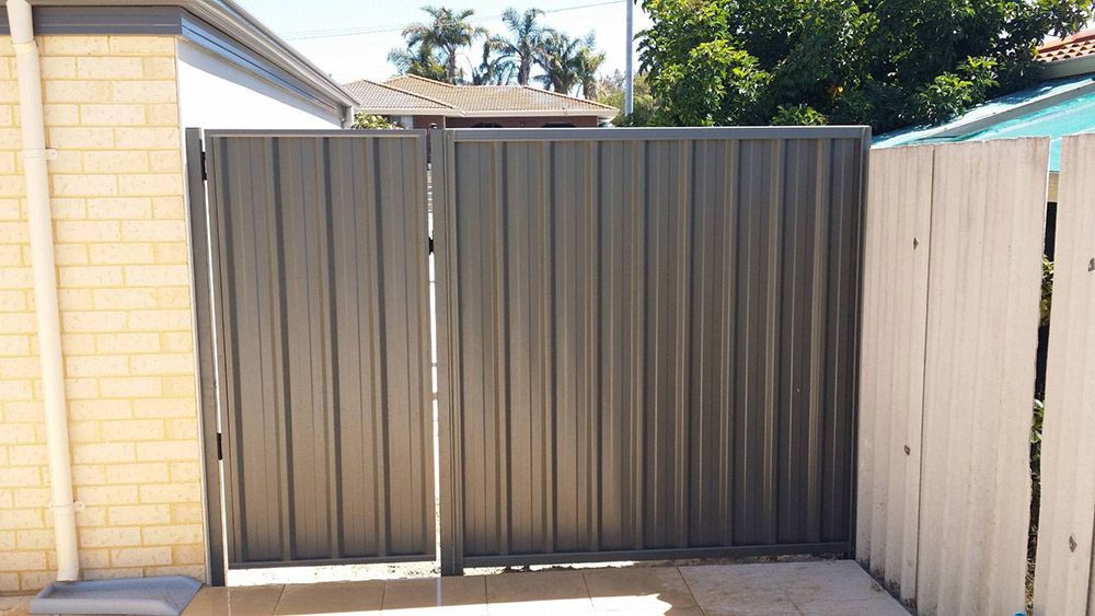 A Metal Gate is Sitting Next to a Wooden Fence — Rearden Fencing Pty Ltd in Toronto, NSW