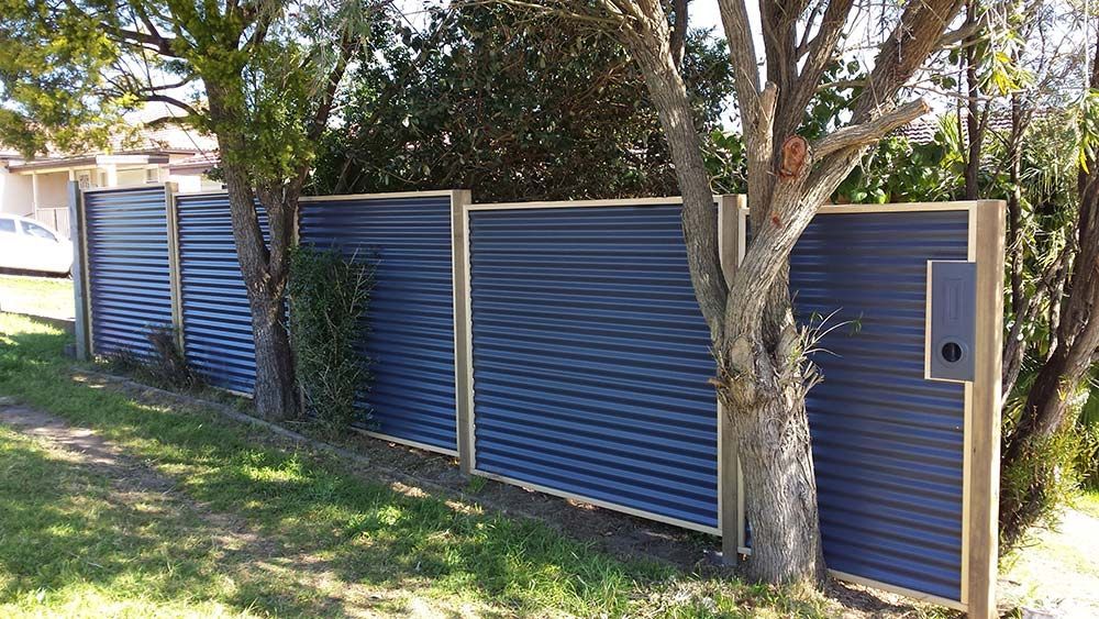 A Blue Fence With a Mailbox in the Middle of It Surrounded by Trees — Rearden Fencing Pty Ltd in Toronto, NSW