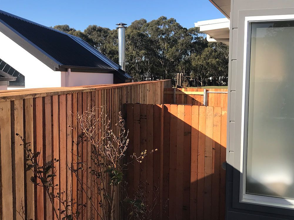 A Wooden Fence Surrounds a Window With a Chimney in the Background — Rearden Fencing Pty Ltd in Toronto, NSW