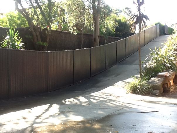A Wooden Fence Surrounds a Driveway With Trees in the Background — Rearden Fencing Pty Ltd in Toronto, NSW