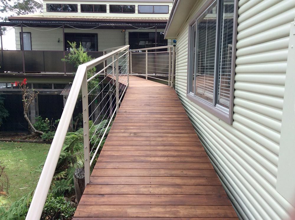 A Wooden Walkway Leading to a House With a Railing — Rearden Fencing Pty Ltd in Toronto, NSW