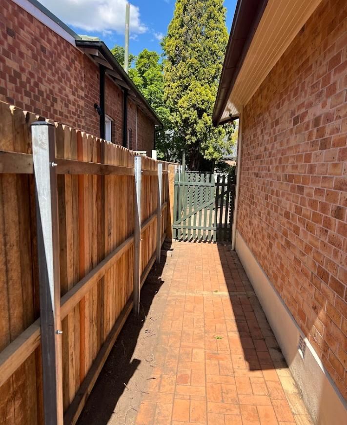 A Wooden Fence Along the Side of A Brick Building — Rearden Fencing Pty Ltd in Toronto, NSW