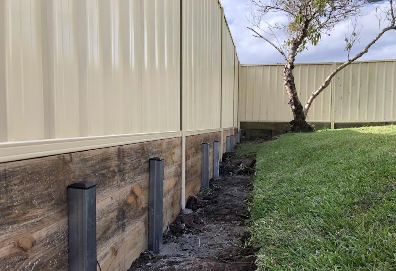 A White Fence Is Surrounded by A Wooden Retaining Wall — Rearden Fencing Pty Ltd in Toronto, NSW