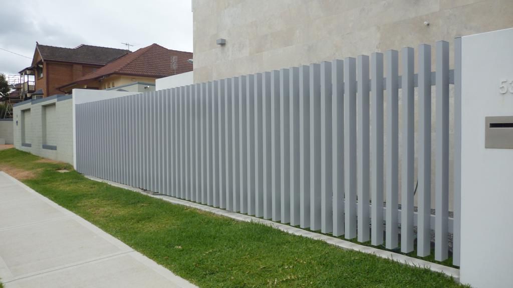 A White Fence Surrounds a Lush Green Yard in Front of A House — Rearden Fencing Pty Ltd in Cessnock, NSW