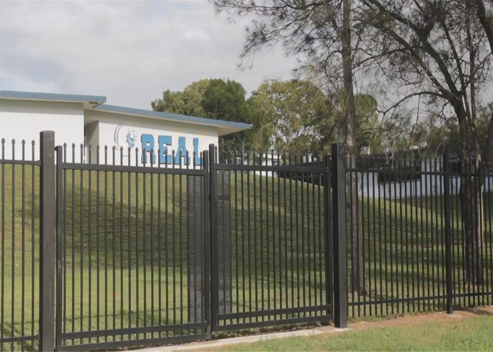 A Fence Surrounds a Building That Says Real on It — Rearden Fencing Pty Ltd in Toronto, NSW