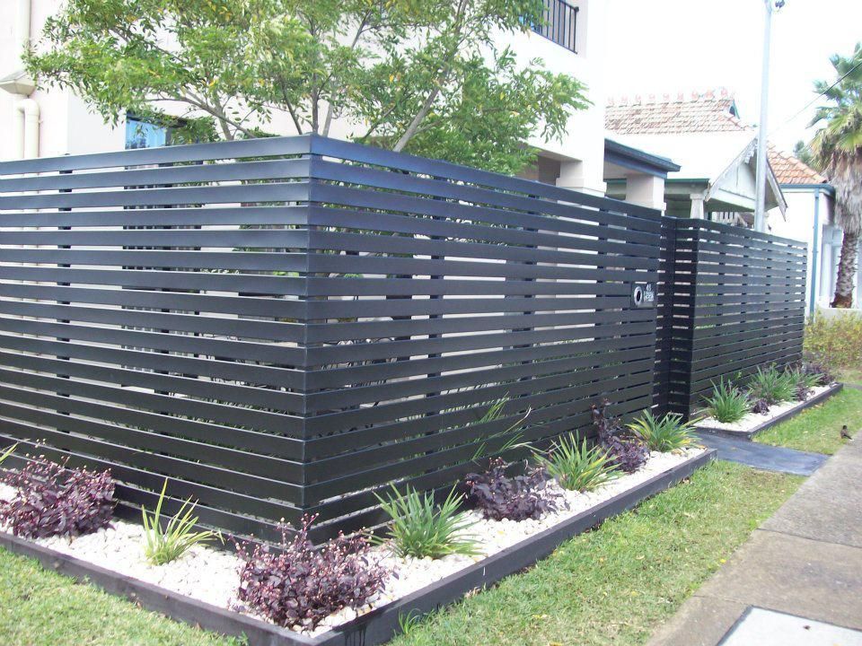 A Black Fence Surrounds a Garden in Front of A House — Rearden Fencing Pty Ltd in Wallsend, NSW