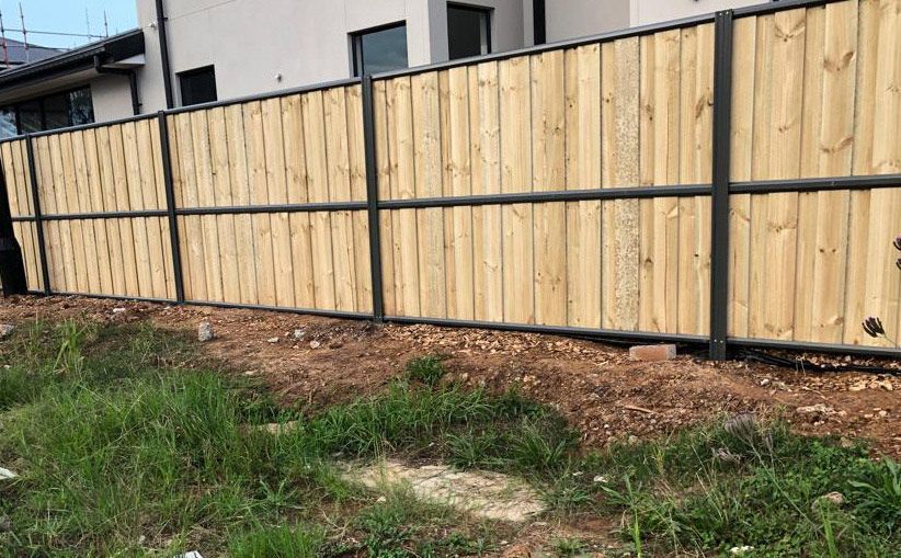 A Wooden Fence is Sitting in the Middle of a Grassy Field Next to a House — Rearden Fencing Pty Ltd in Toronto, NSW