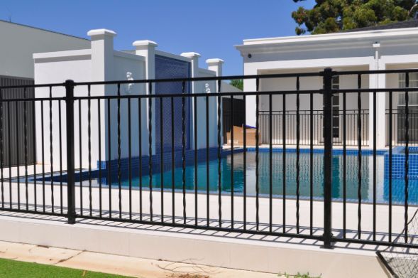 A Black Fence Surrounds a Swimming Pool in Front of a House — Rearden Fencing Pty Ltd in Toronto, NSW