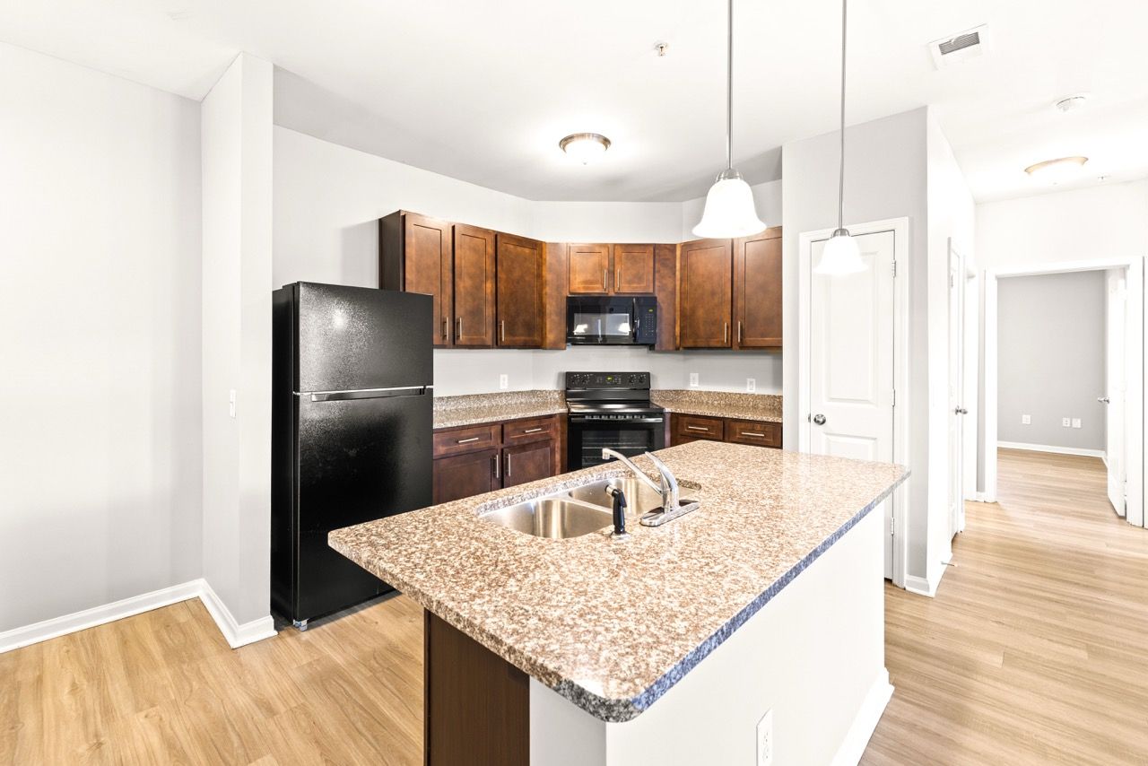 Modern apartment kitchen with granite countertops, dark wood cabinets, and black appliances.