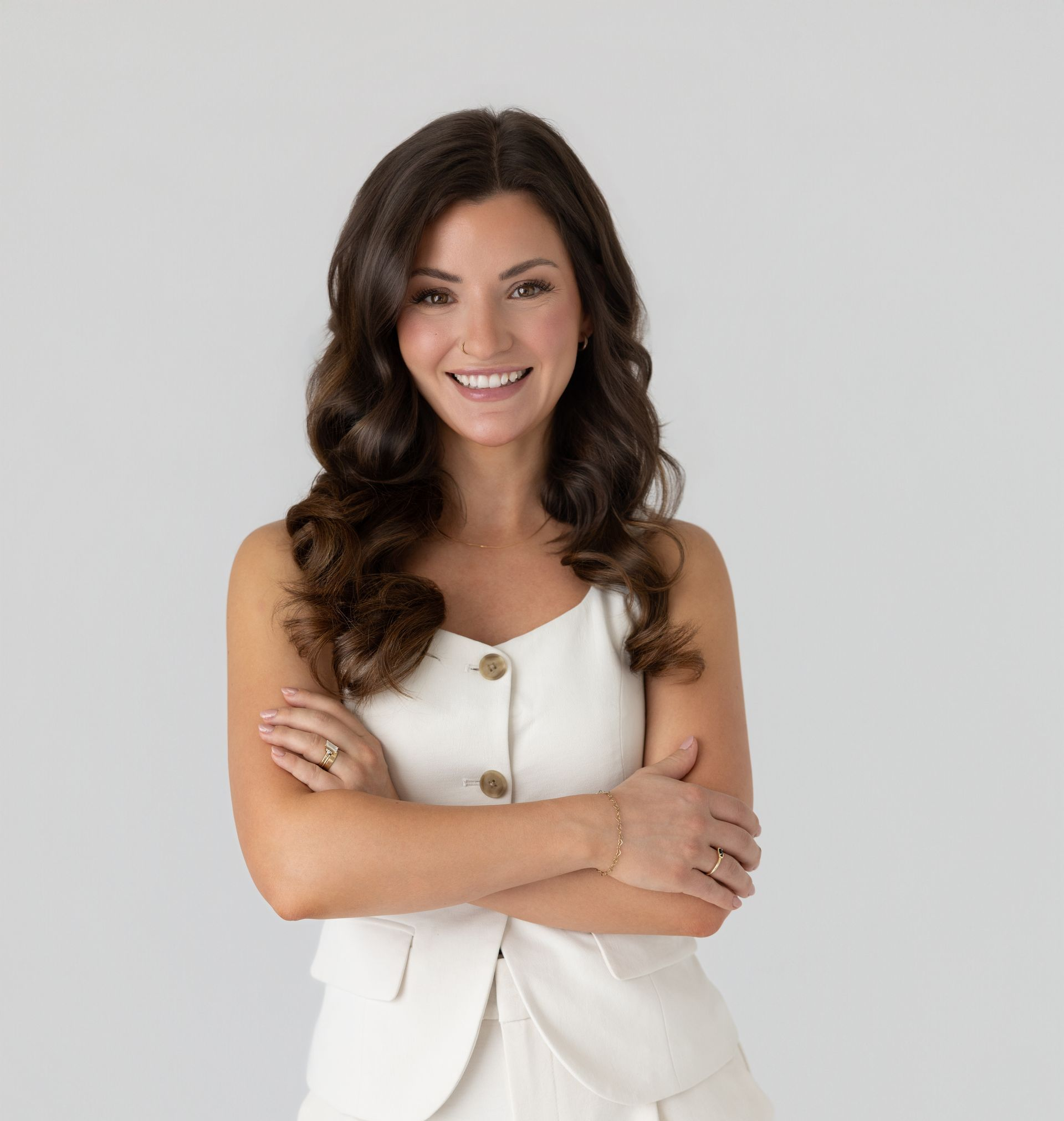 Smiling woman in a white sleeveless suit, arms crossed, against a light gray background