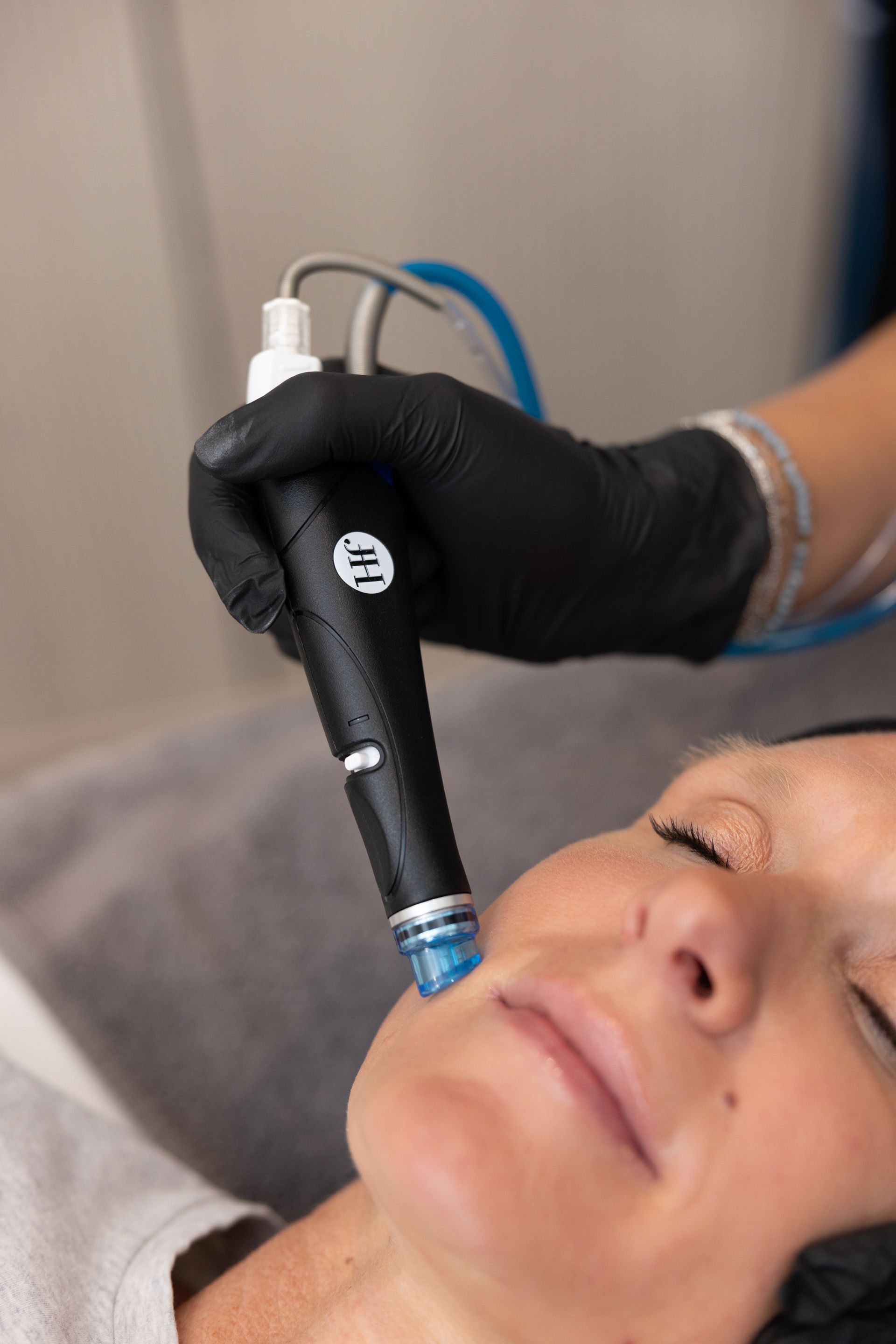 Gloved hand using a handheld device on a woman's face during a cosmetic facial treatment