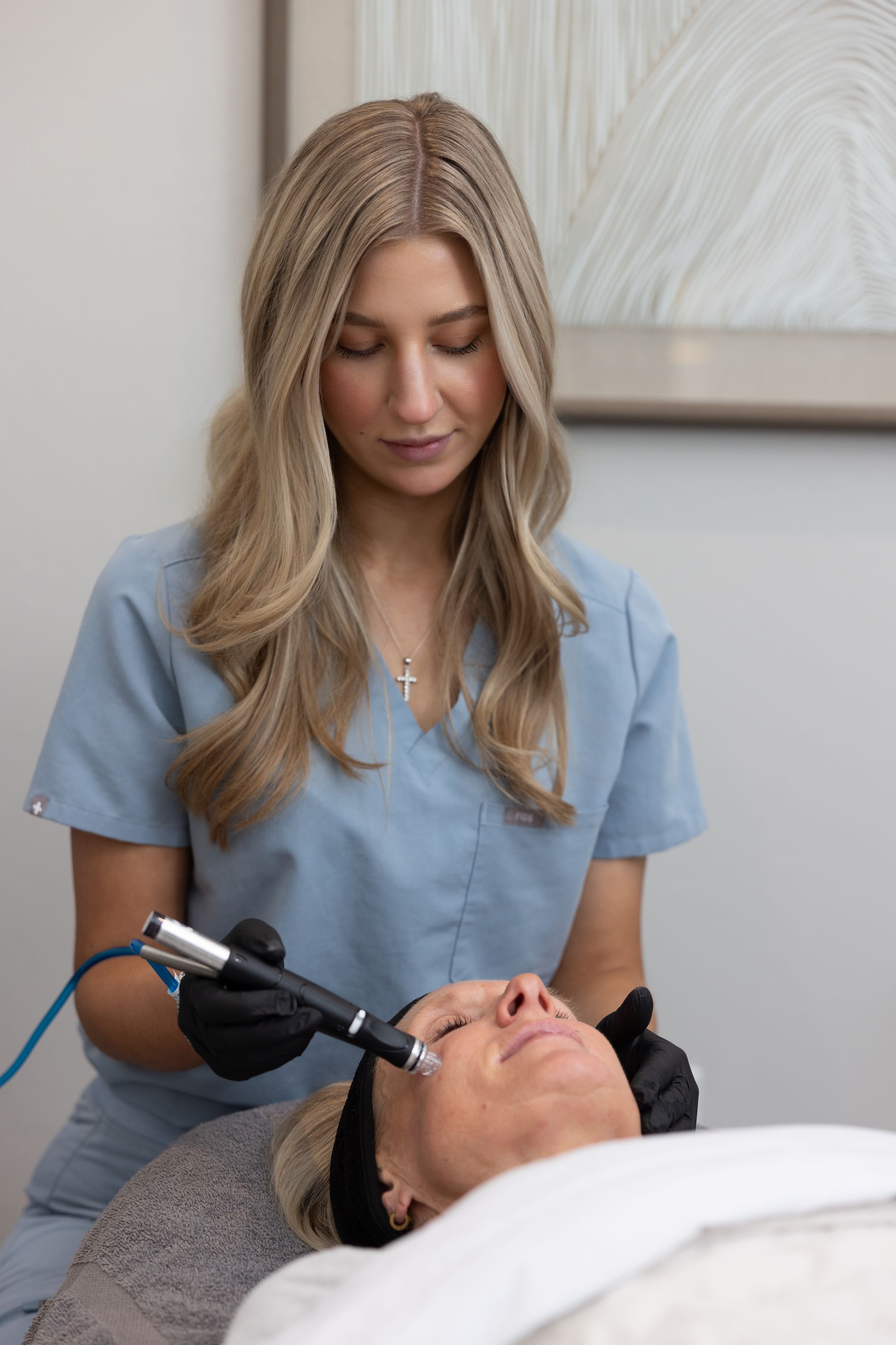 Aesthetic clinician using a facial device on a reclining client in a spa treatment room
