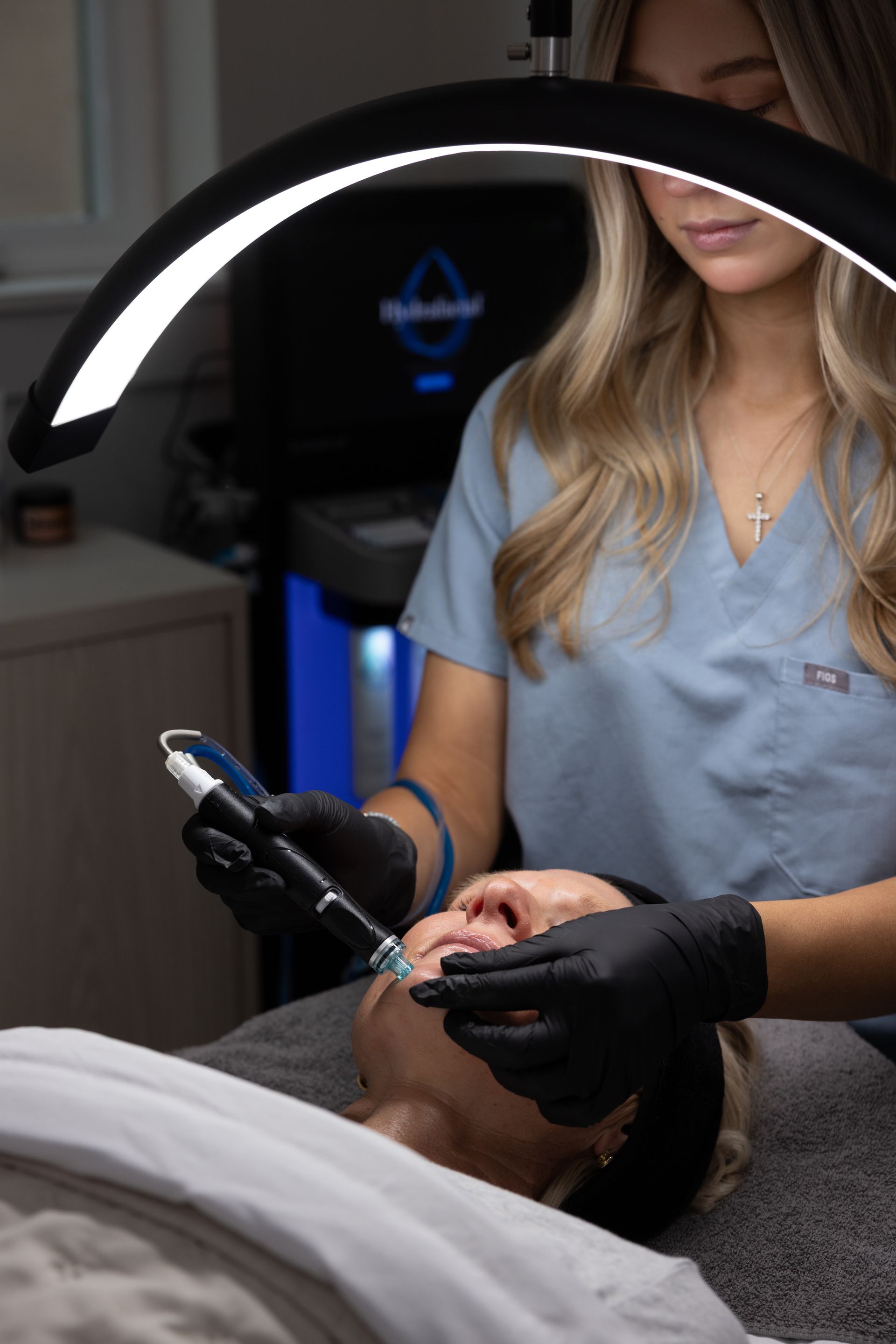 Technician performing a handheld skincare treatment under a ring light in a spa treatment room
