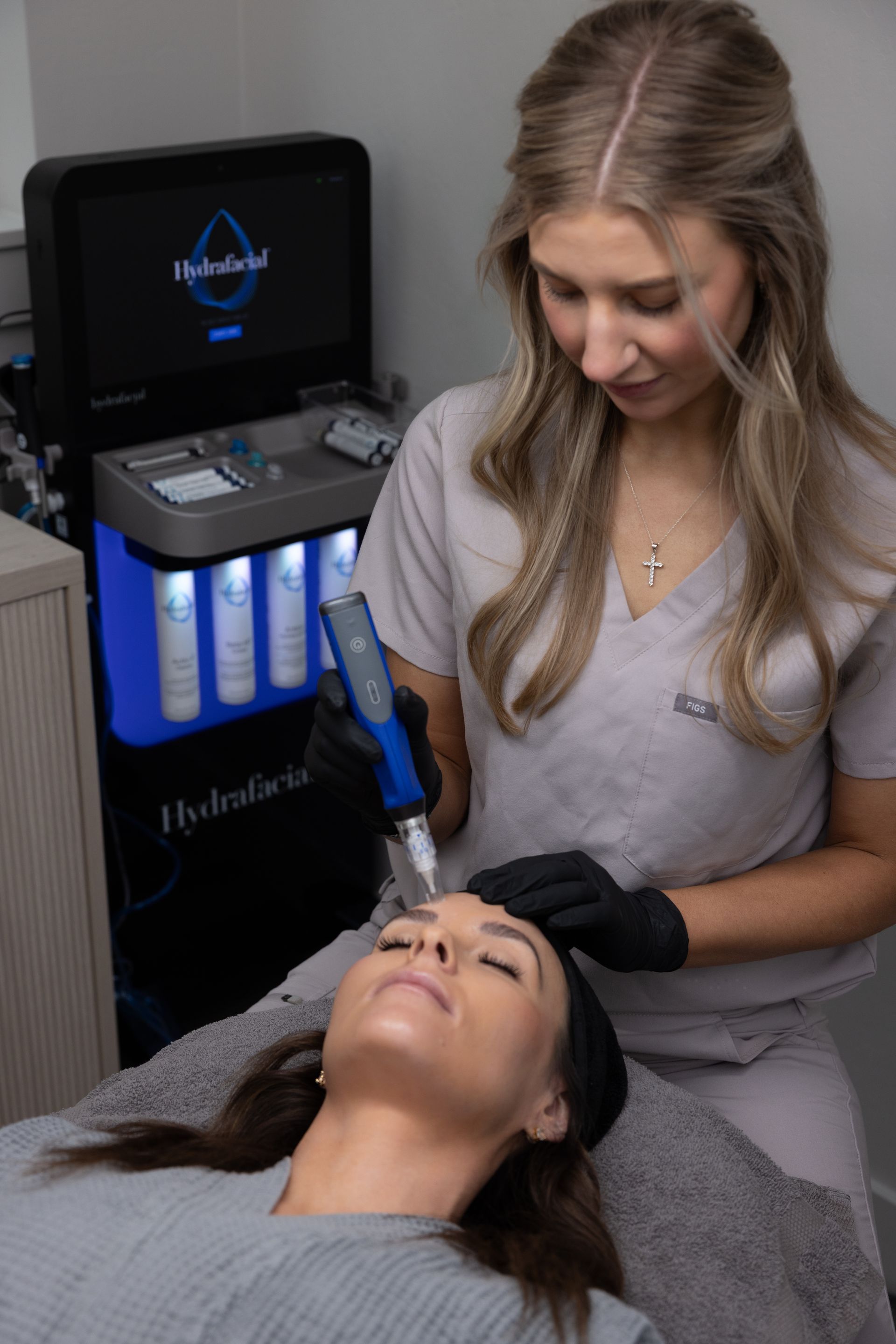 Esthetician applying facial treatment with a blue device to a client in a spa room
