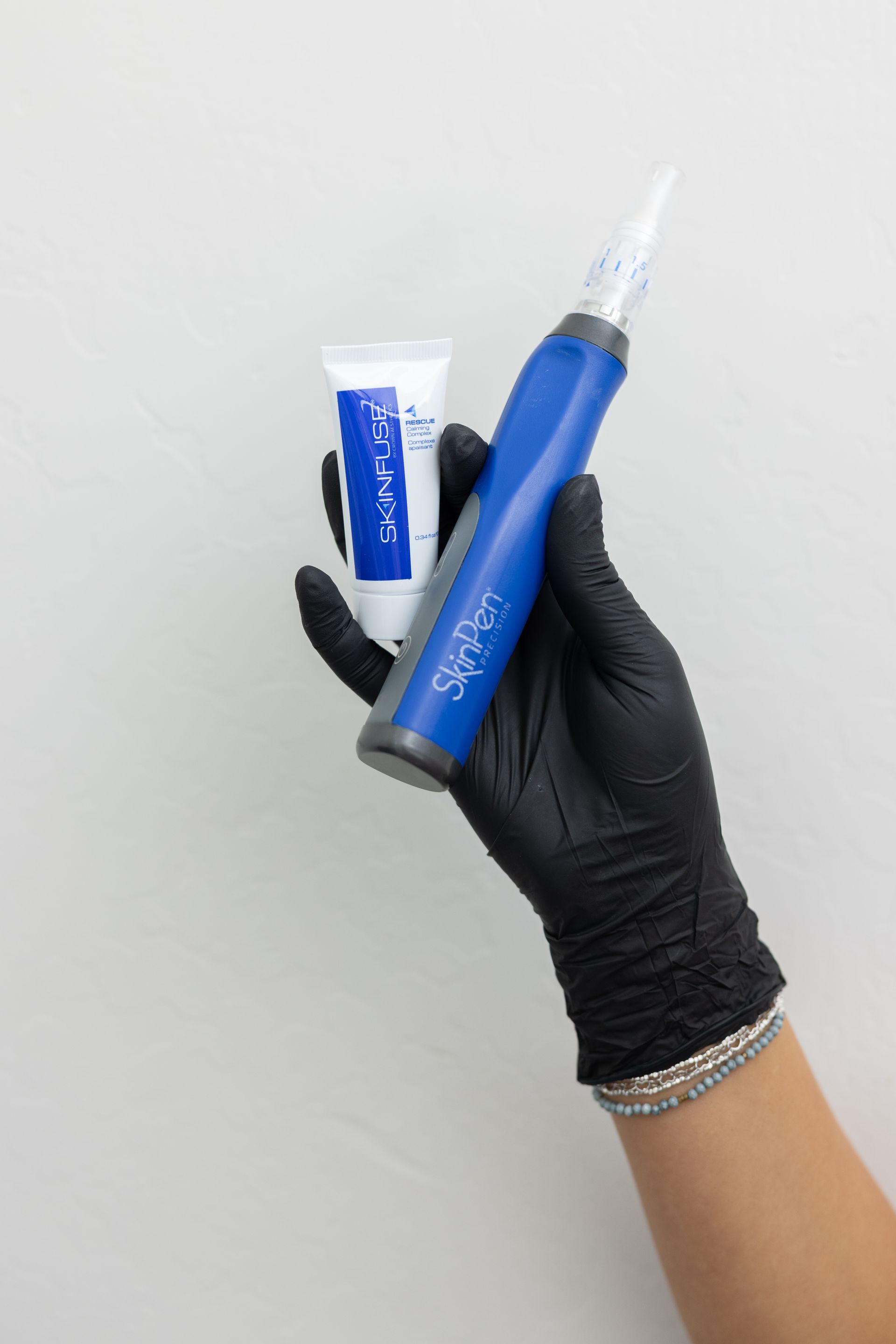 Person in blue scrubs performing a cosmetic facial treatment on a reclined client with a handheld device.