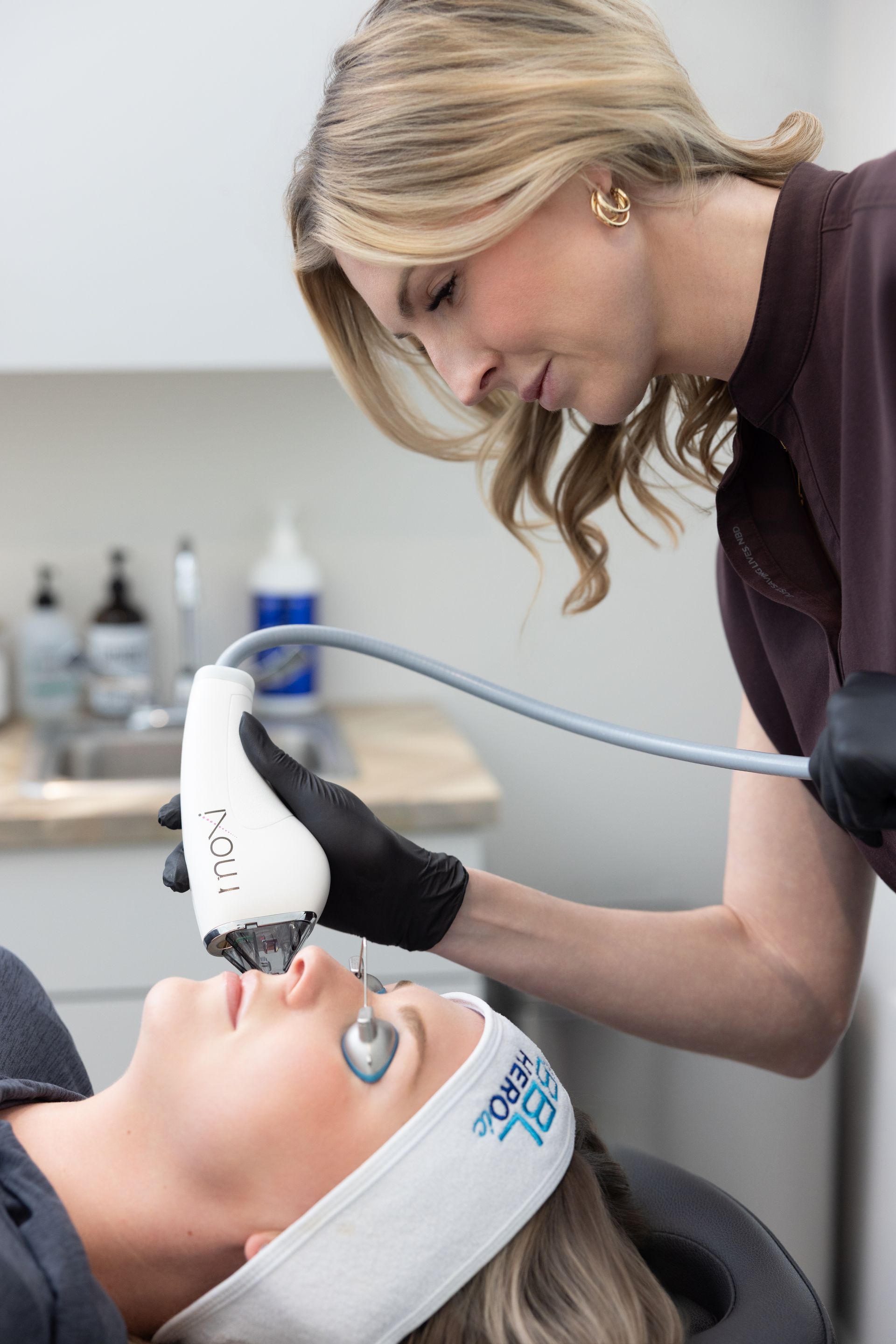 A clinician uses a handheld device on a patient lying back in a treatment room.