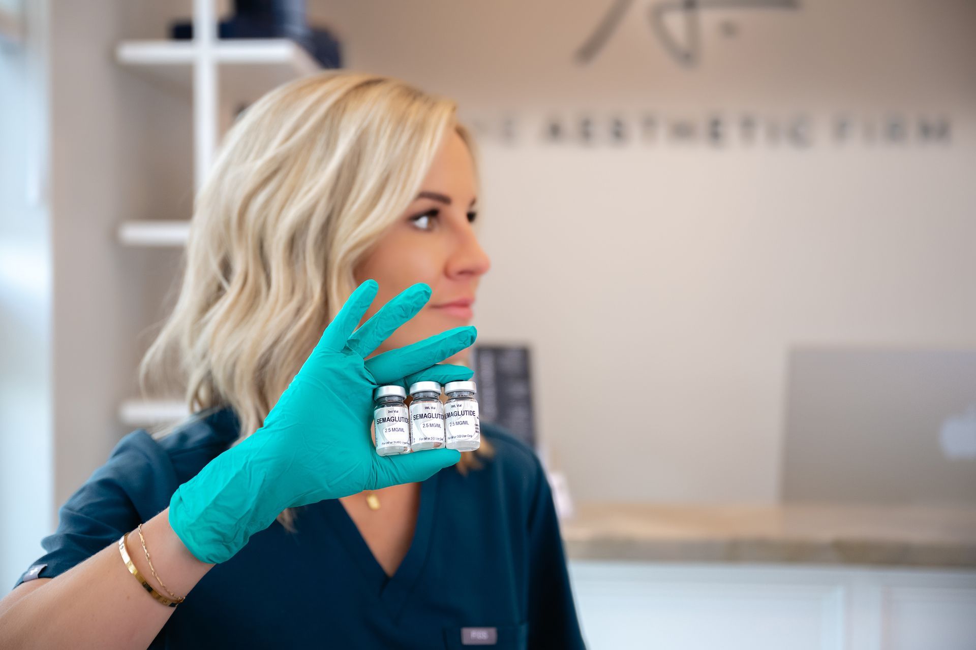 Woman in teal scrubs and gloves holding a clear dental aligner in a clinic lobby
