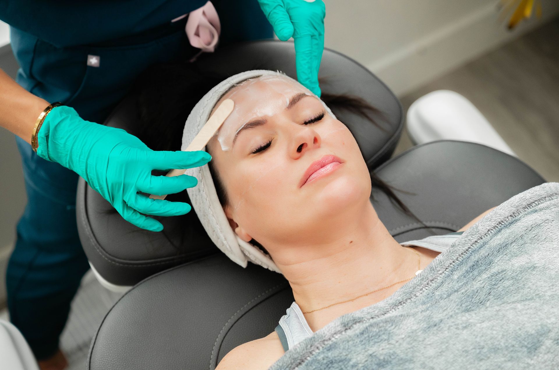 A facial treatment is being applied to a reclining client by gloved hands in a spa setting