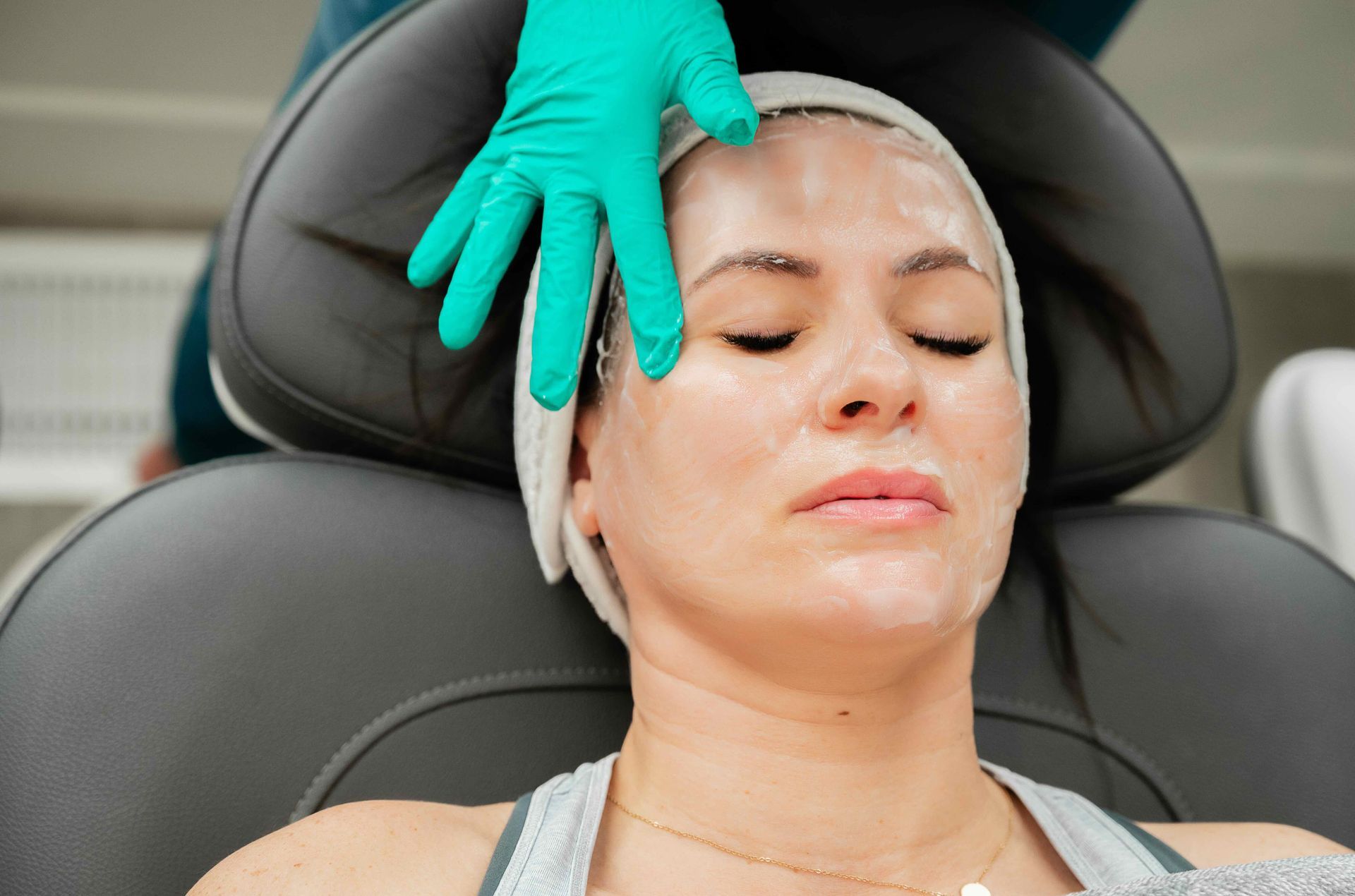 Facial treatment in progress, with a gloved hand applying product to a reclining client’s face