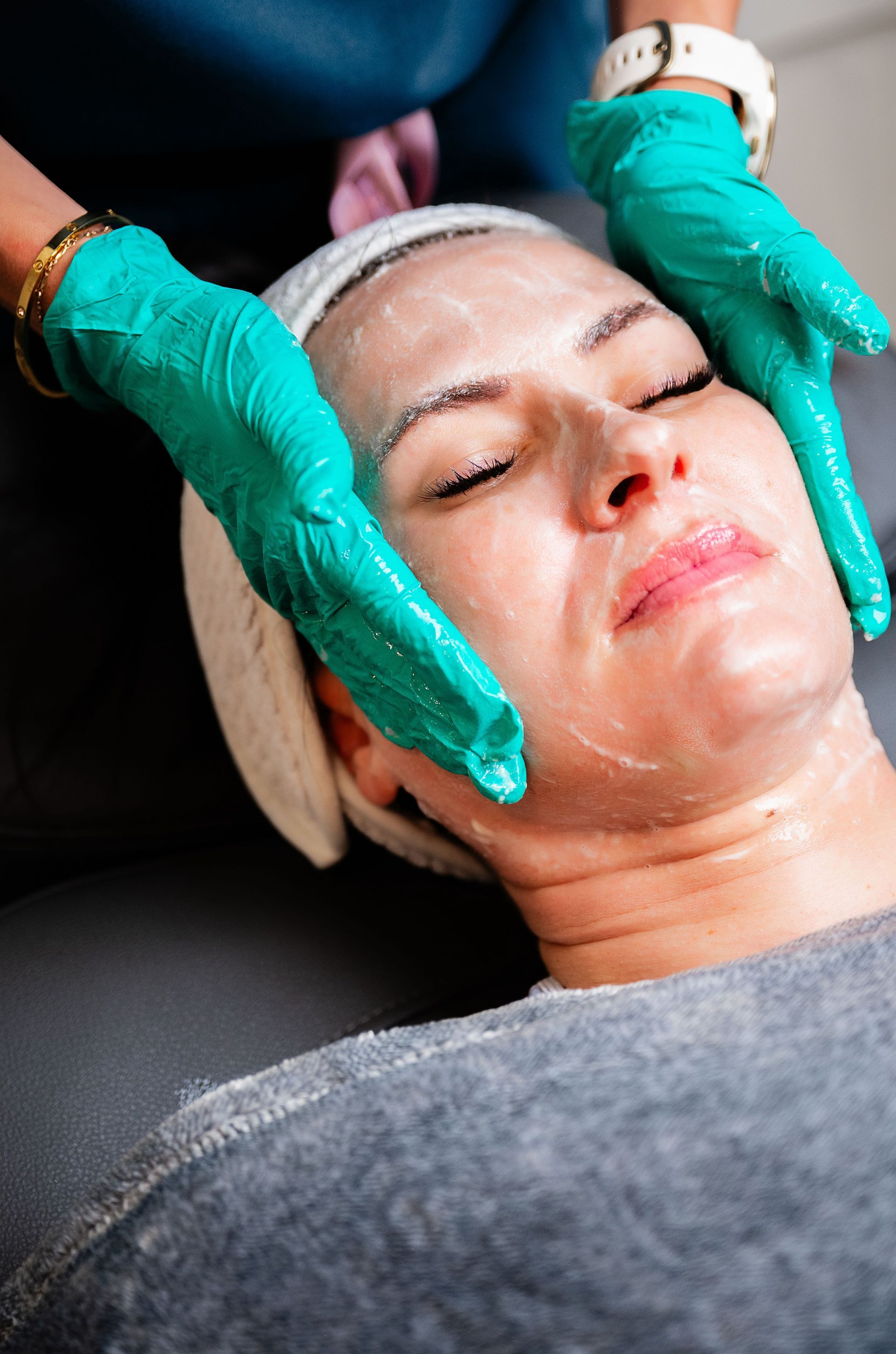 Facial treatment in progress, with gloved hands applying cream to a woman’s face.