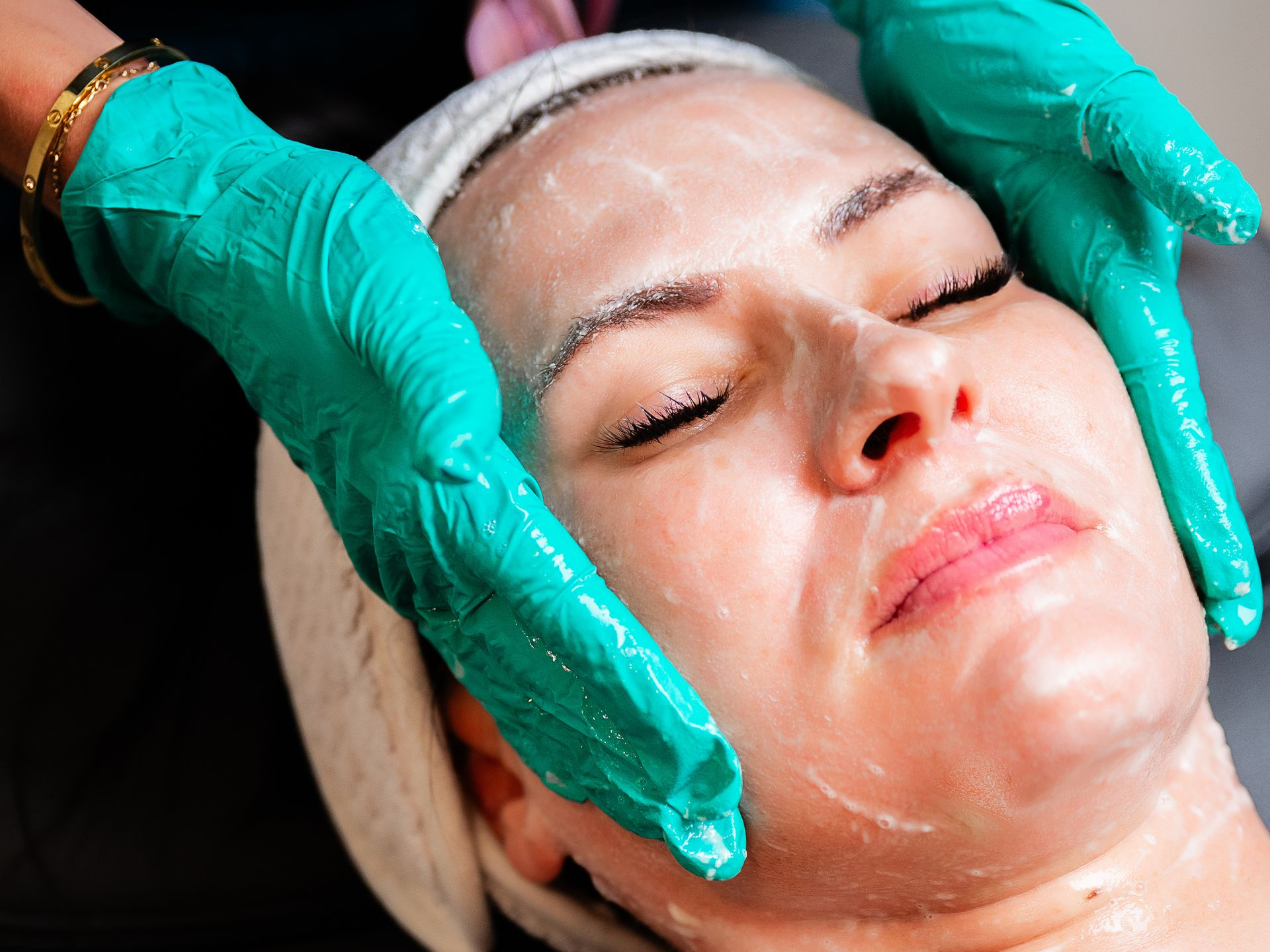 Gloved hands massage a woman’s face with skincare cream during a facial treatment