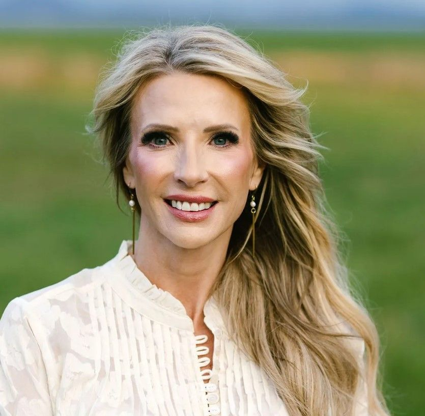 Portrait of a smiling woman in a white blouse outdoors with a blurred green field background