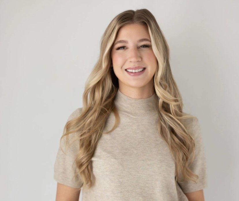 Smiling blonde person in a beige sweater against a light gray background