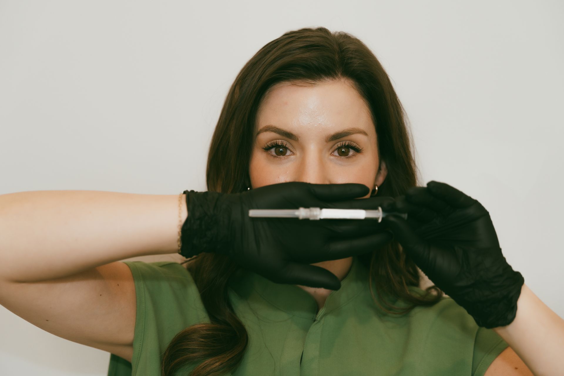 Person wearing black gloves holds a pen horizontally in front of their face against a plain background.