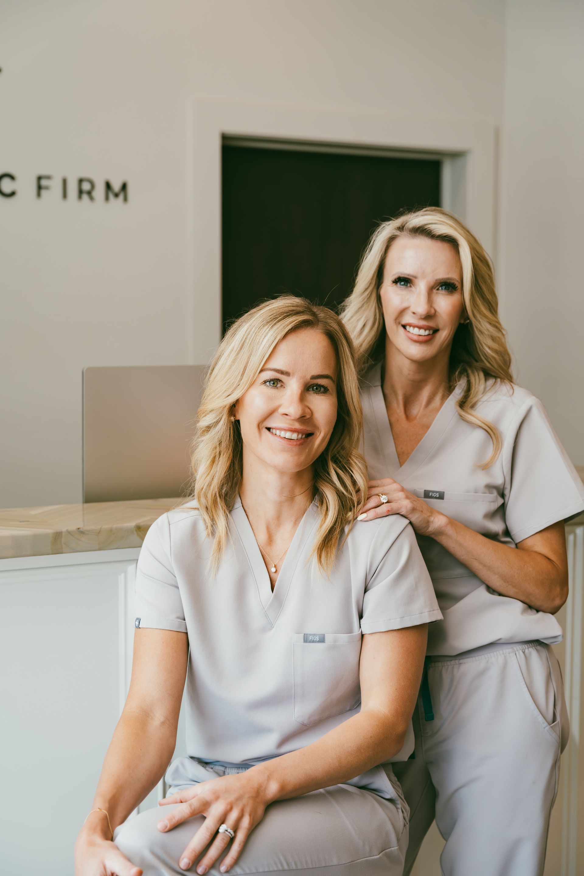 Two smiling women in white uniforms at a clinic reception desk