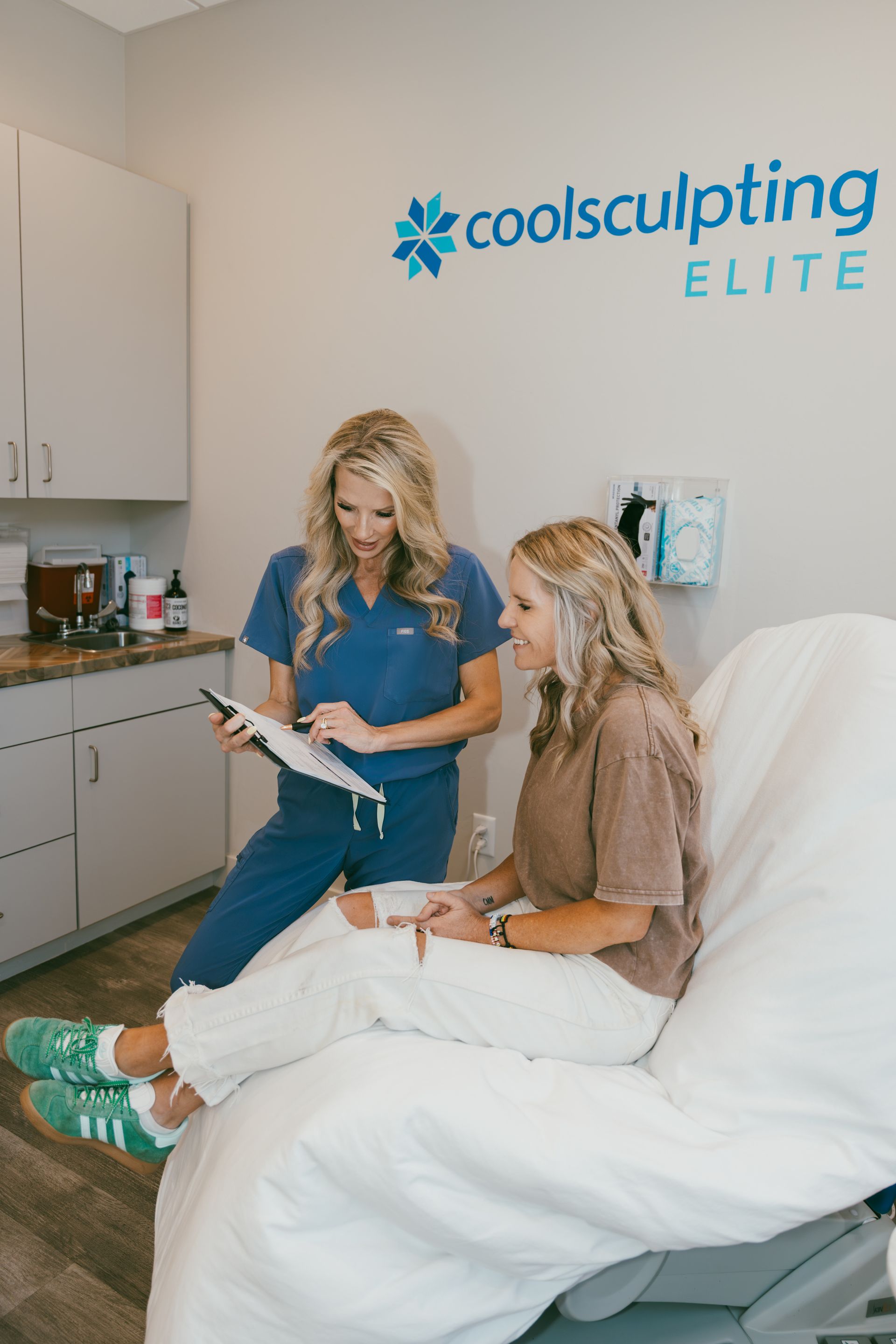 Medical consultation in a CoolSculpting Elite clinic, with a clinician and client seated on a treatment chair.