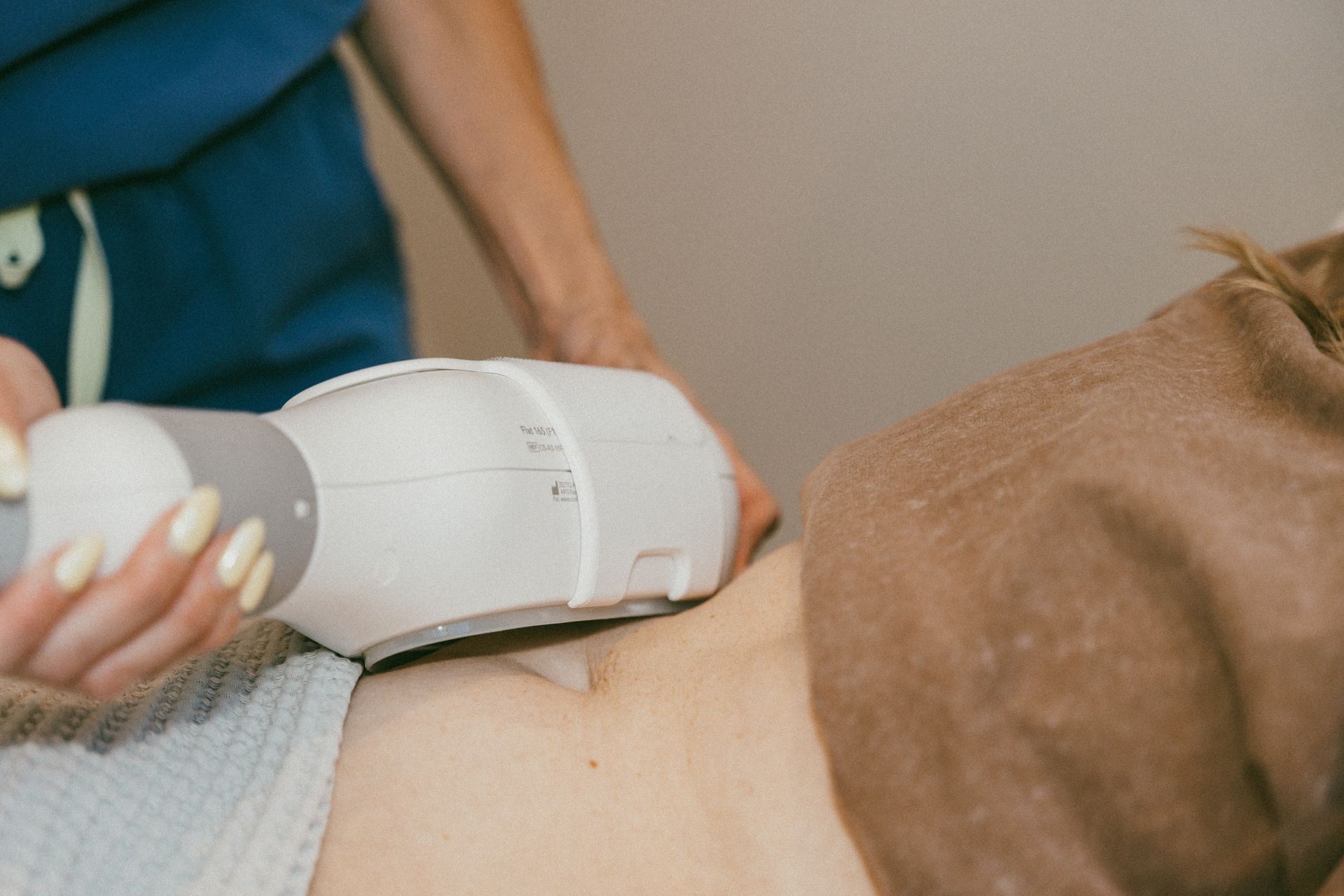 Hand holding a white skincare device against a person’s bare side on a bed