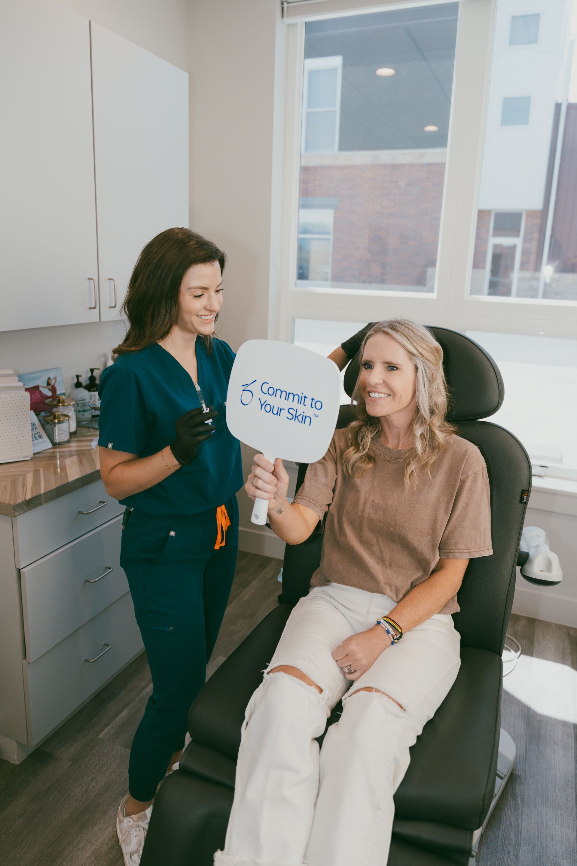 Patient holding a sign while seated in a clinic chair, with a dental professional standing beside her.