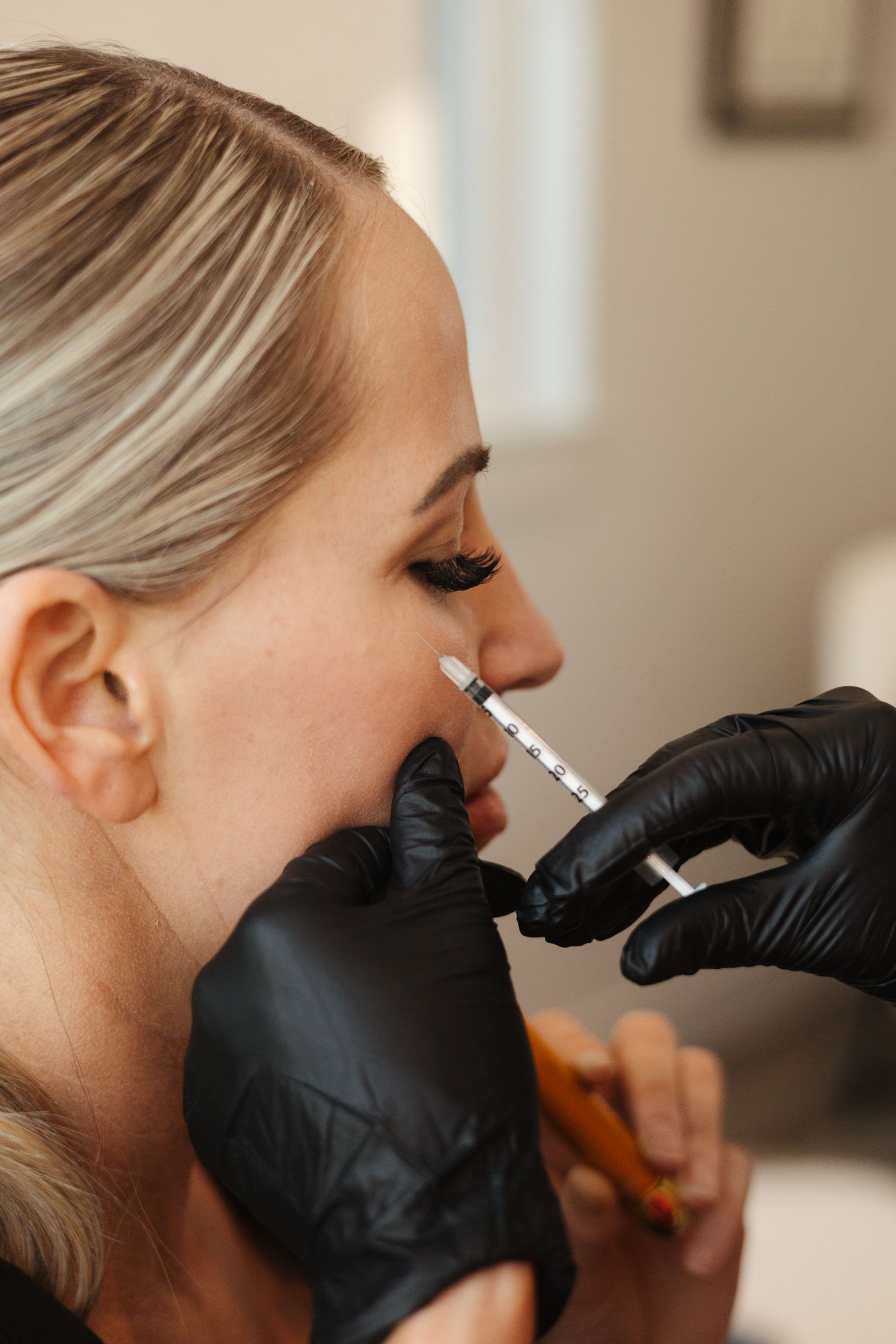 Gloved hands applying a facial treatment with a syringe to a woman’s cheek in a spa setting