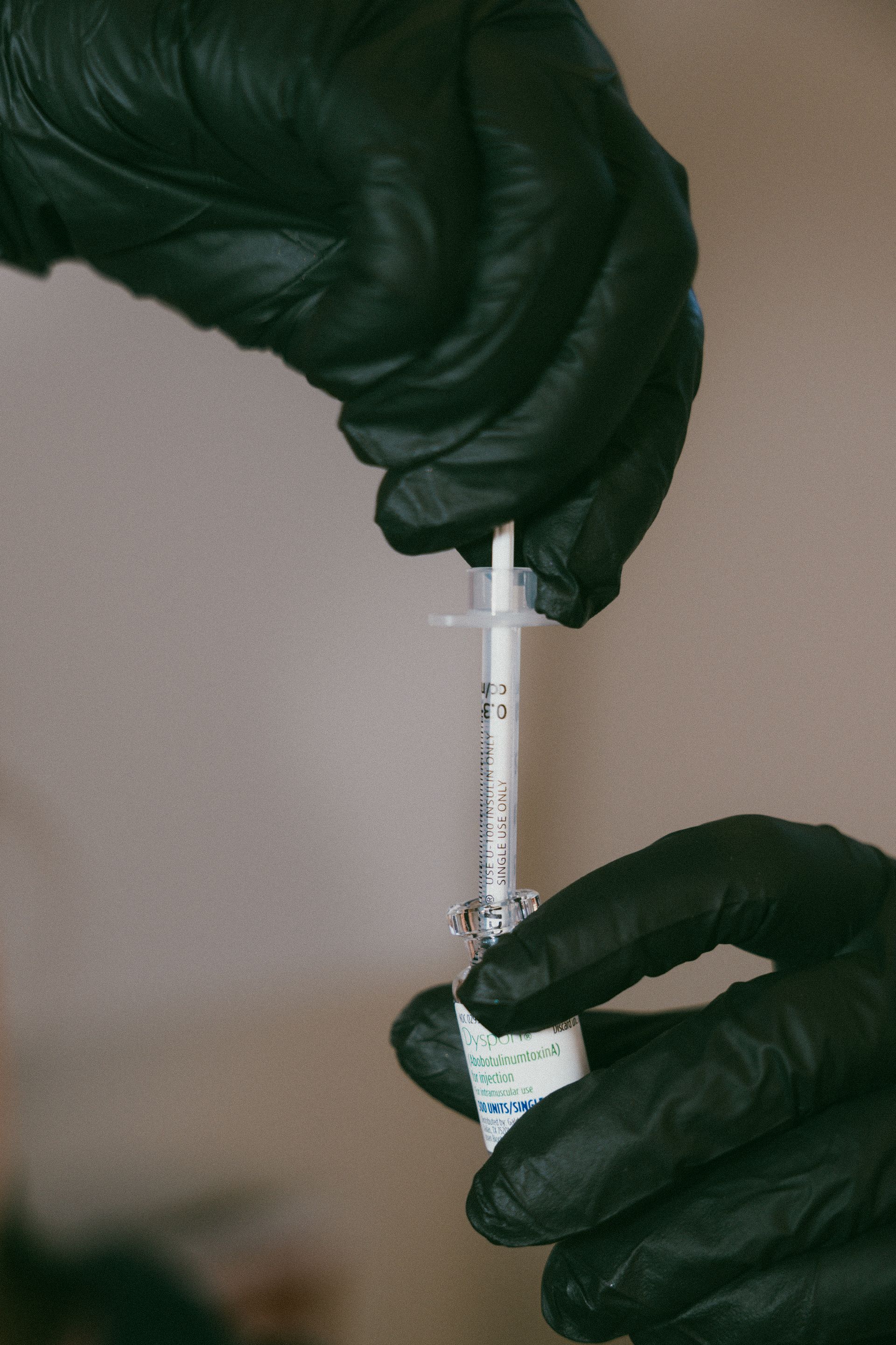 Gloved hands holding a syringe with clear liquid against a beige background